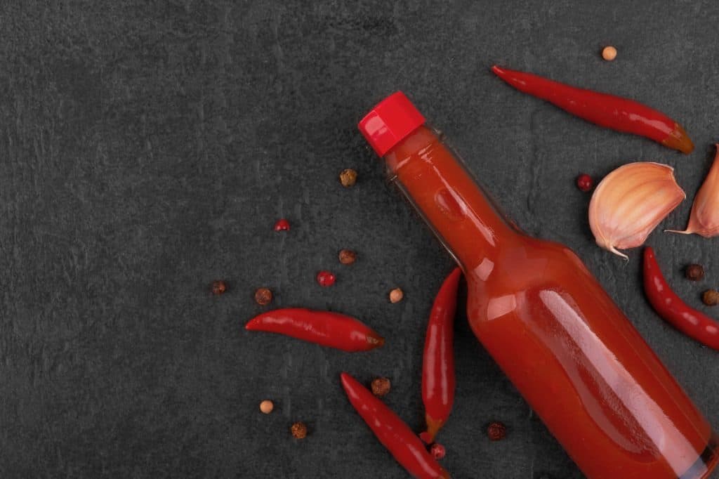 a bottle of hot sauce surrounded by peppers on a dark grey background