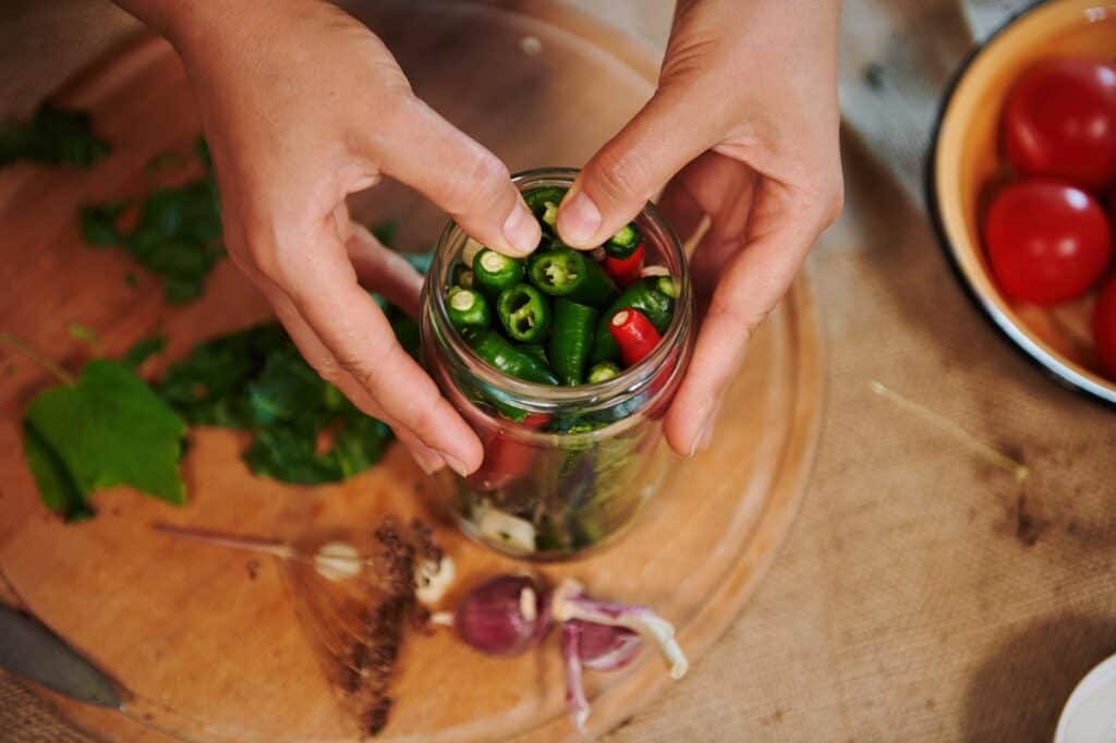 hands packing peppers into a glass canning jar