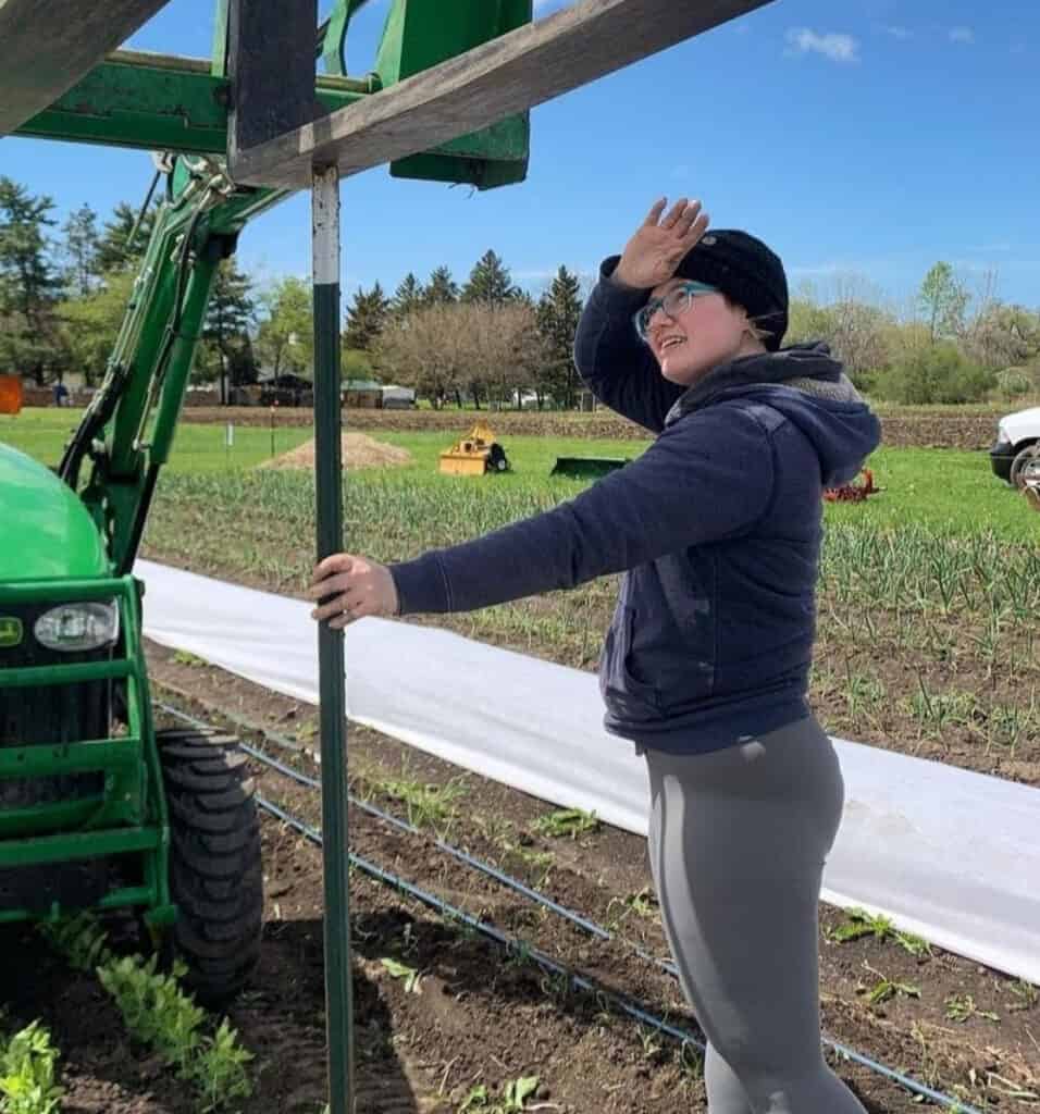 photo of annie holding up a T-post with a tractor pushing it into the ground.