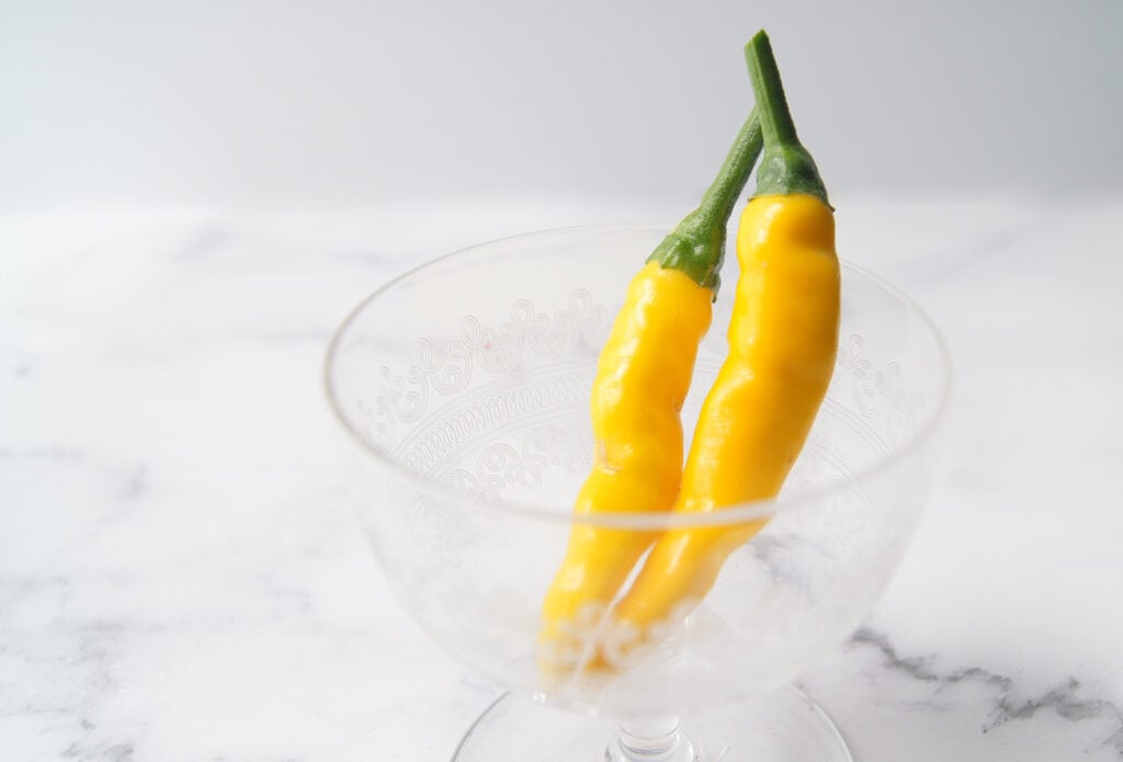 two yellow kristian peppers in a glass on a marble background.