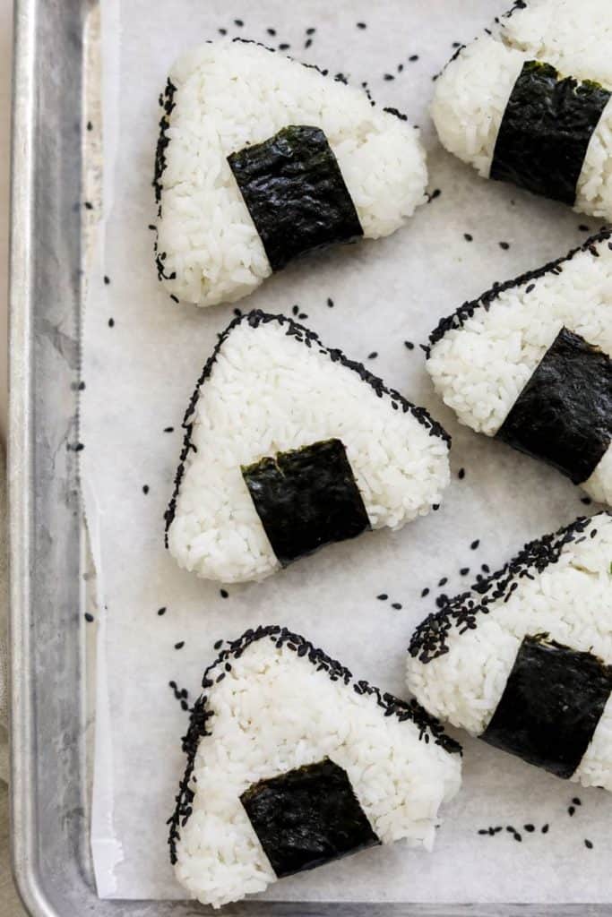 six onigiri on a metal sheet lined with paper.