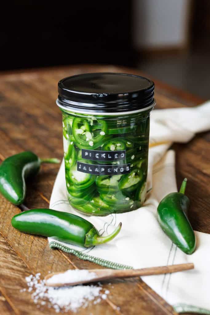 small jar of jalapeno rings with three jalapenos around it.