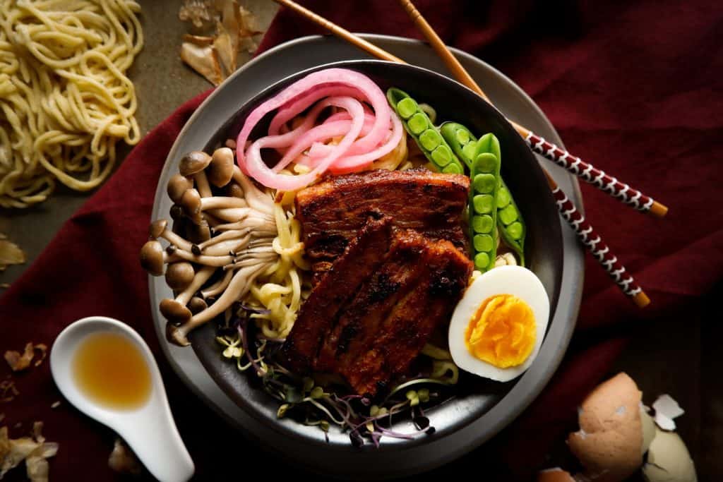 bowl of ramen topped with pork belly, peas, egg, and mushroom.