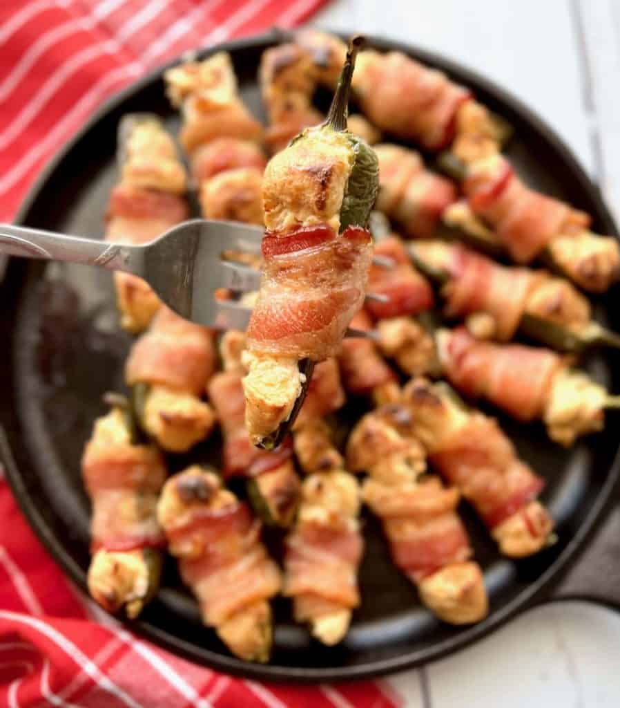 fork holding up a smoked jalapeño popper with blurred tray of poppers in the background.