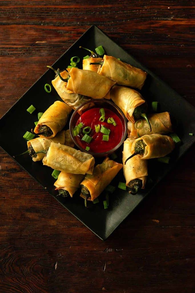 jalapeno peppers wrapped in spring roll papper arranged around a sauce dish.