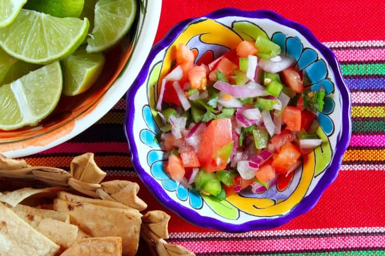 a bowl of pico de gallo, lime wedges, and chips