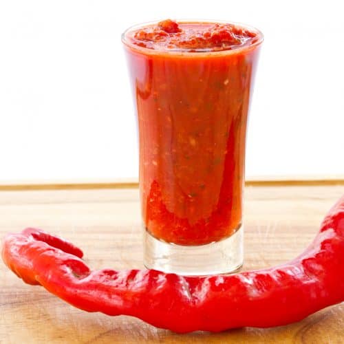 a shot glass full of hot sauce with a chili pepper in front